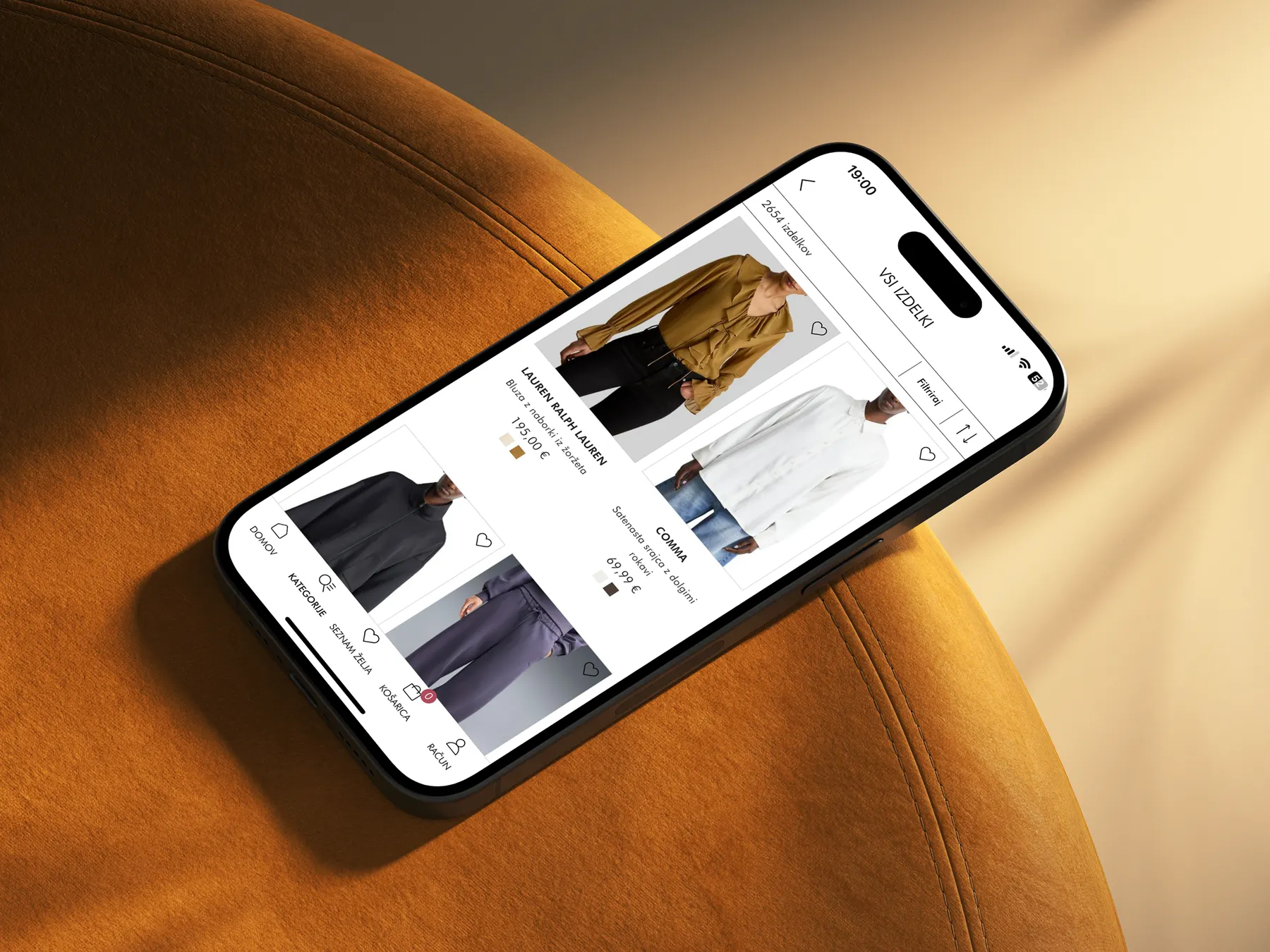 The Emporium app on a phone resting on an ochre velvet chair: a product grid with brands and prices